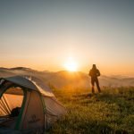 Un campeur profite du lever du soleil dans un décor de montagne avec sa tente. Une escapade nature idéale.