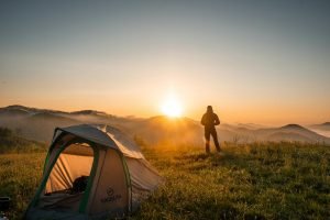 Un campeur profite du lever du soleil dans un décor de montagne avec sa tente. Une escapade nature idéale.