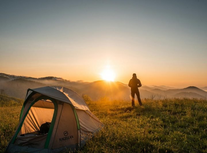 Un campeur profite du lever du soleil dans un décor de montagne avec sa tente. Une escapade nature idéale.